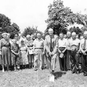 Group of white people standing around white man with shovel