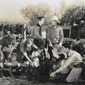 White men and women dressed as cowfolk surrounding a young man on the ground