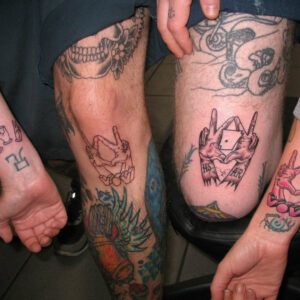 Arms and legs with tattoos showing two hands making a sign with two V's