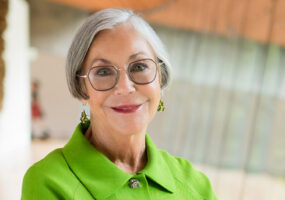 Older white woman smiling in green suit and glasses with earrings