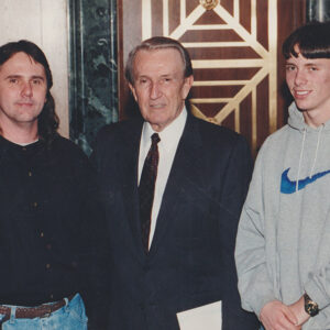 Older white man in suit standing between two younger white men