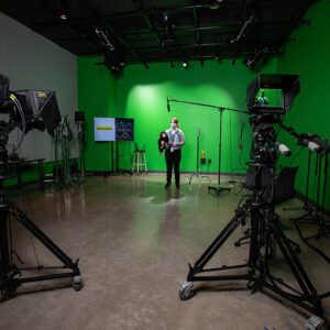 White woman with chimpanzee puppet standing by green wall in video studio in front of cameras