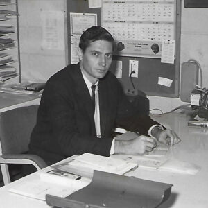 White man in suit and tie seated at desk