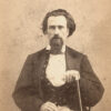 Bearded white man sitting and holding a cane