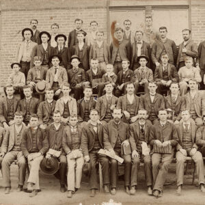 Five rows of young men posing for photo in front of brick building