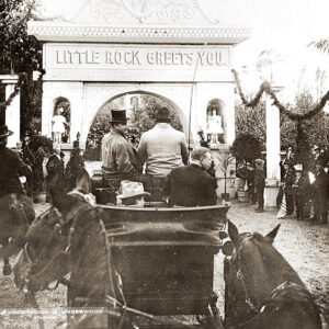 White men in horse drawn carriage waving by an arch that says "Little Rock Greets You"
