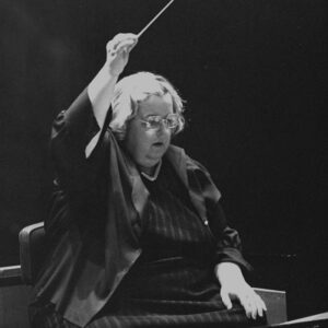 Older white woman in glasses holding a baton over her head