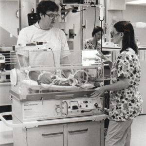 White man and white woman examining baby in incubator