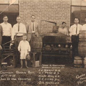 White men and one boy standing around a moonshine still and barrels